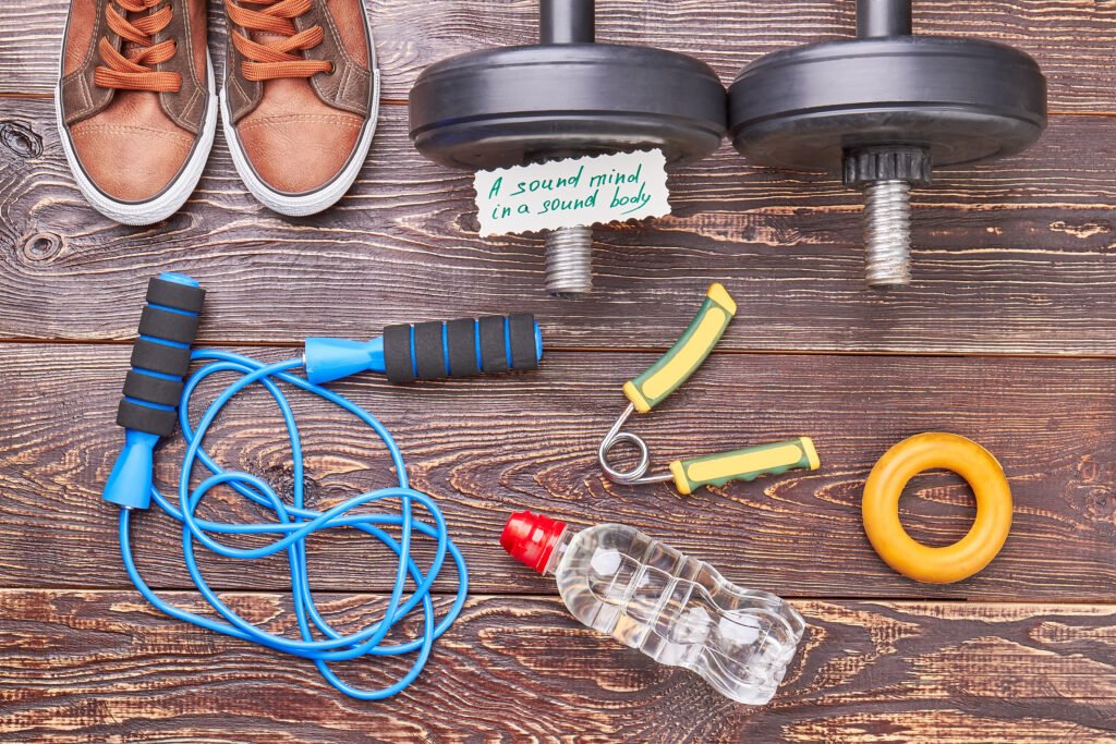 Gym equipment background. Expanders, jumping rope, dumbbells, shoes, water, message on rustic wooden background.